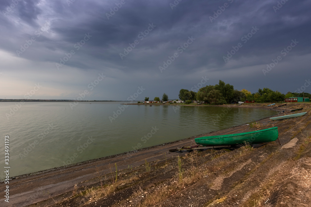 Lake Musov - green fishing boat on the shore of the lake with dramatic heavy clouds in the sky