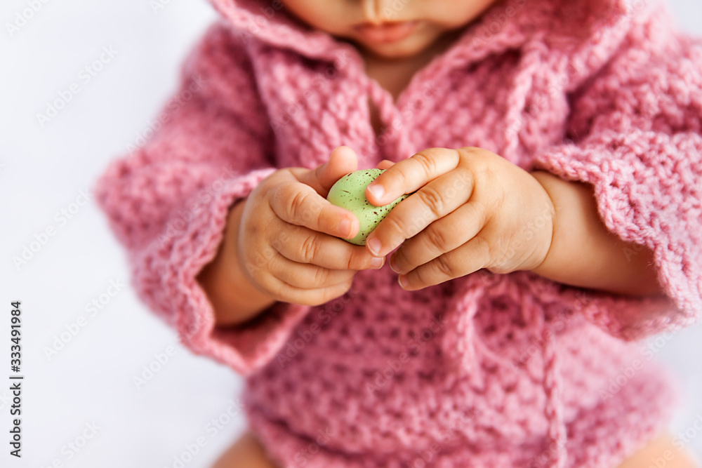 Little baby girl in pink romper playing with green Easter egg , closeup of tiny hands Little baby girl in pink romper playing with green Easter egg , closeup of tiny hands