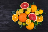citrus fruits, half grapefruits, lemons, oranges, limes with green leaves lie on a brown wooden table. view from above