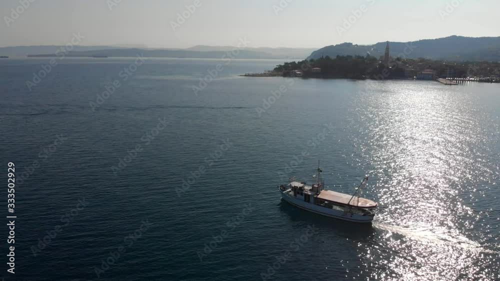 Aerial circle shot of fishing boat with coastal town in background, sunny day Aerial circle shot of fishing boat with coastal town in background, sunny day