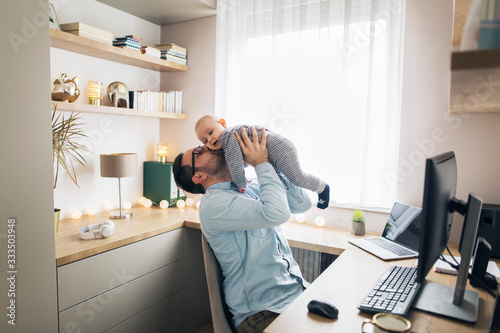 Young father working from home and babysitting his baby boy.