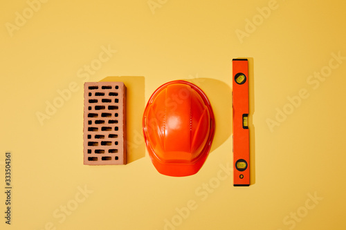 top view of brick, orange helmet and spirit level on yellow background photo