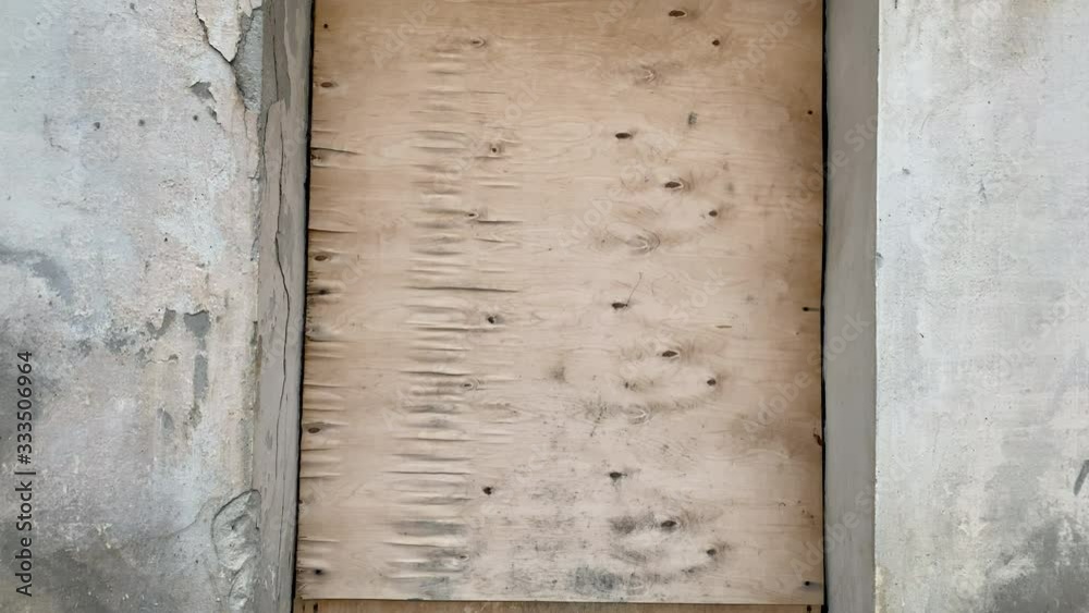Old abandoned house, stone wall with window boarded up by plywood shield.
