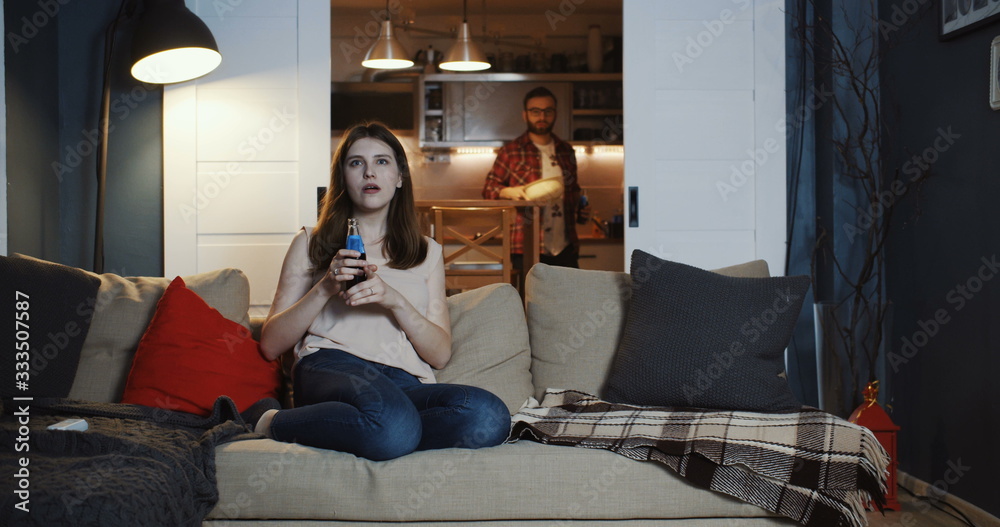 Obraz premium Happy young Caucasian romantic couple sit together for a relaxed movie night at home with snacks and drinks slow motion.
