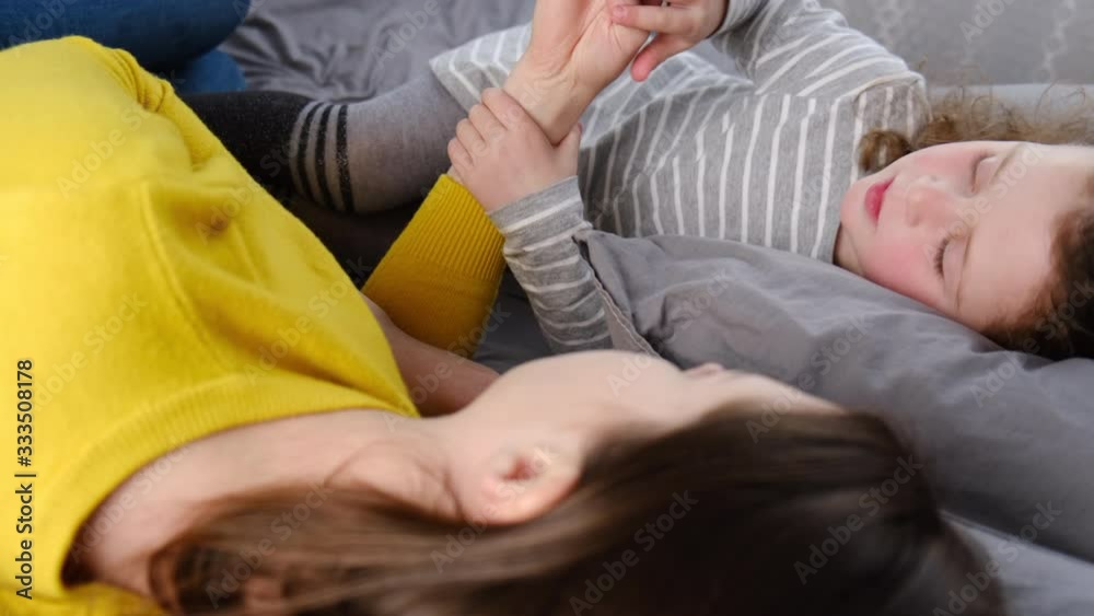 Close up of a happy loving young mother and cute small child daughter playing and counting with fingers, lying in bed face to face, enjoying active leisure free time in bedroom. Close up of a happy loving young mother and cute small child daughter playing and counting with fingers, lying in bed face to face, enjoying active leisure free time in bedroom.