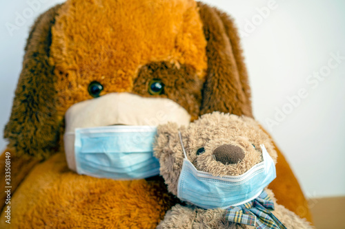 Two brown teddy bears - small and big - wearing protective blue masks