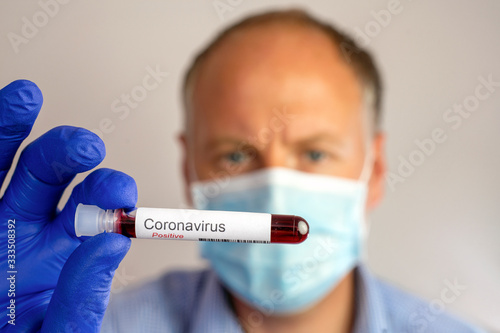 A serious man wearing protective mask and showing positive result of coronavirus test.