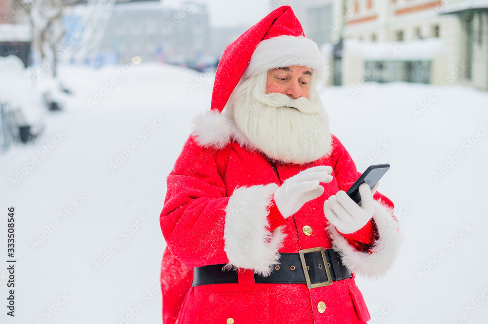 Portrait of a funny funky fat modern Santa Claus use his mobile phone. An elderly man in a suit before Christmas communicates on a smartphone. Portrait of a funny funky fat modern Santa Claus use his mobile phone. An elderly man in a suit before Christmas communicates on a smartphone.
