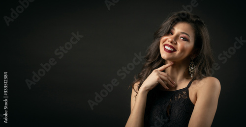 Half-body portrait of luxurious-looking lady with bright make-up touching neck over black background with copyspace