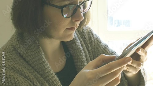 Young caucasian woman in cardigan and casual clothes wearing black frame eyeglasses and using tablet at home