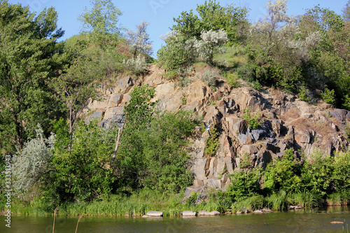 Former stone quarry. Nature Restoration. Summer landscape with river, rocks, green grass, trees and blue sky.