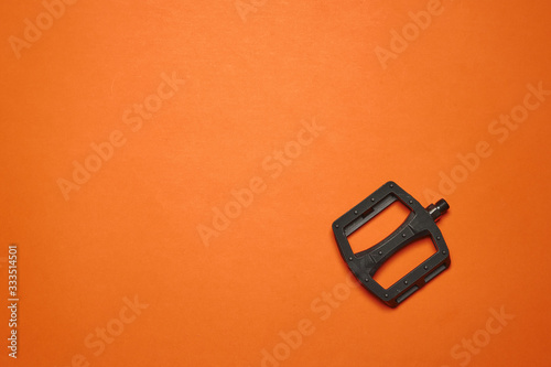 The pedal of the BMX bike lies on an orange background. Spare parts for extreme bike. Minimalism.