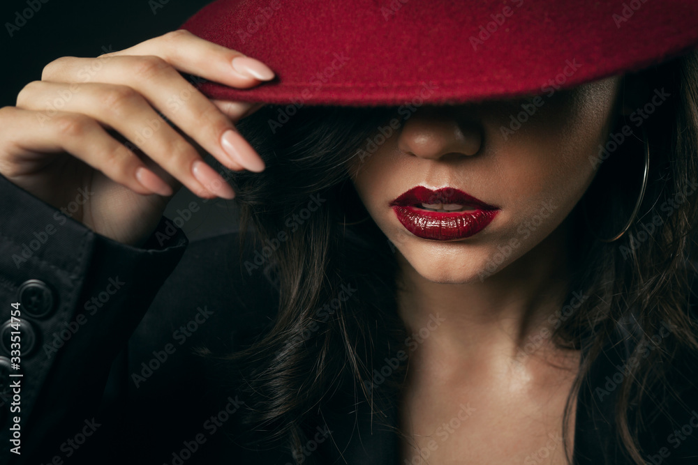 Cropped shot of sensual glamorous woman hiding face under hat touching maroon wide brim, retro style Cropped shot of sensual glamorous woman hiding face under hat touching maroon wide brim, retro style