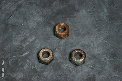 Three small rusty nuts lie next in the shape of a triangle on a dark gray background with a beautiful texture. Industrial photophone for design and text.