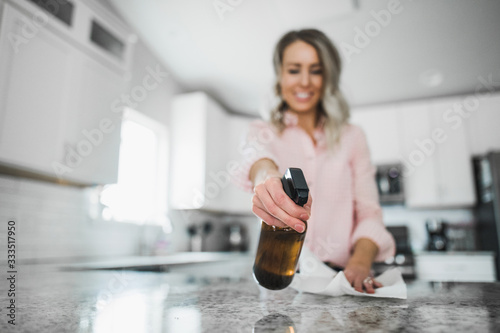 Young woman cleaning her kitchen couters with disinfectant spray bottle