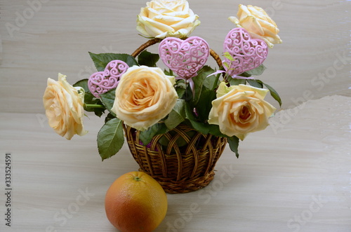  On a white background, a basket with fresh pink roses, decorative, openwork hearts, on the table is a grapefruit.