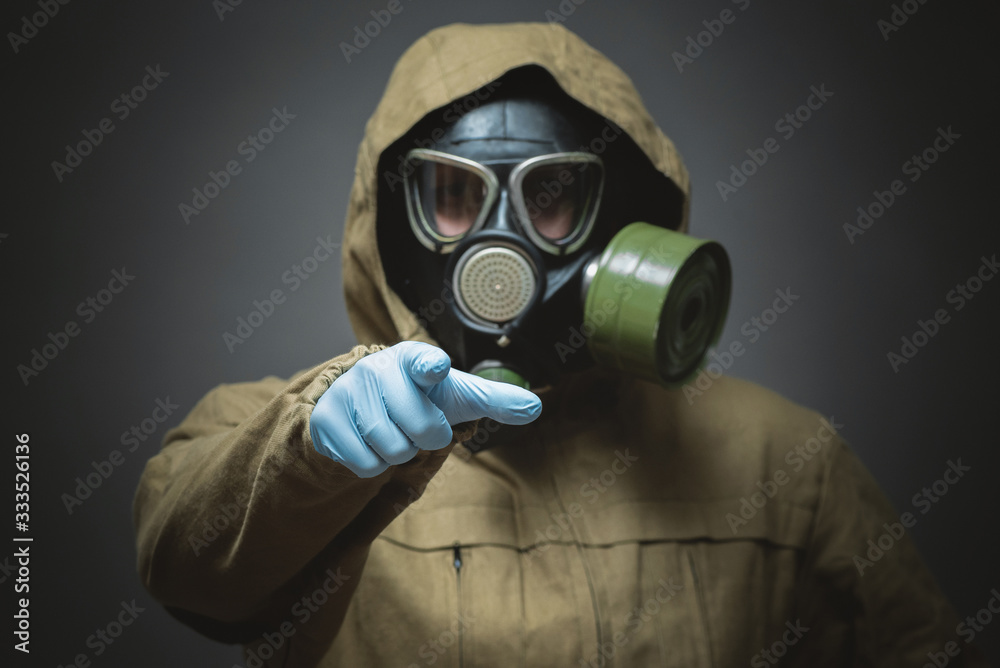 Man in gas mask is showing ahead by his index finger close up on gray background. Man in gas mask is showing ahead by his index finger close up on gray background.