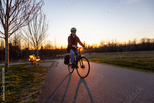 Caucasian Woman Riding a Bicycle on a Pedestrian Path during a sunny sunset. Taken in Surrey, Vancouver, British Columbia, Canada.