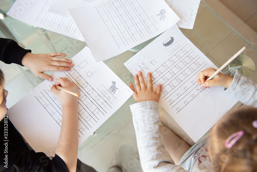 Schoolboy and schoolgirl writing letters. Close-up  pencil in the hand of child. Children learning to write letters at the table. A home distance learning.