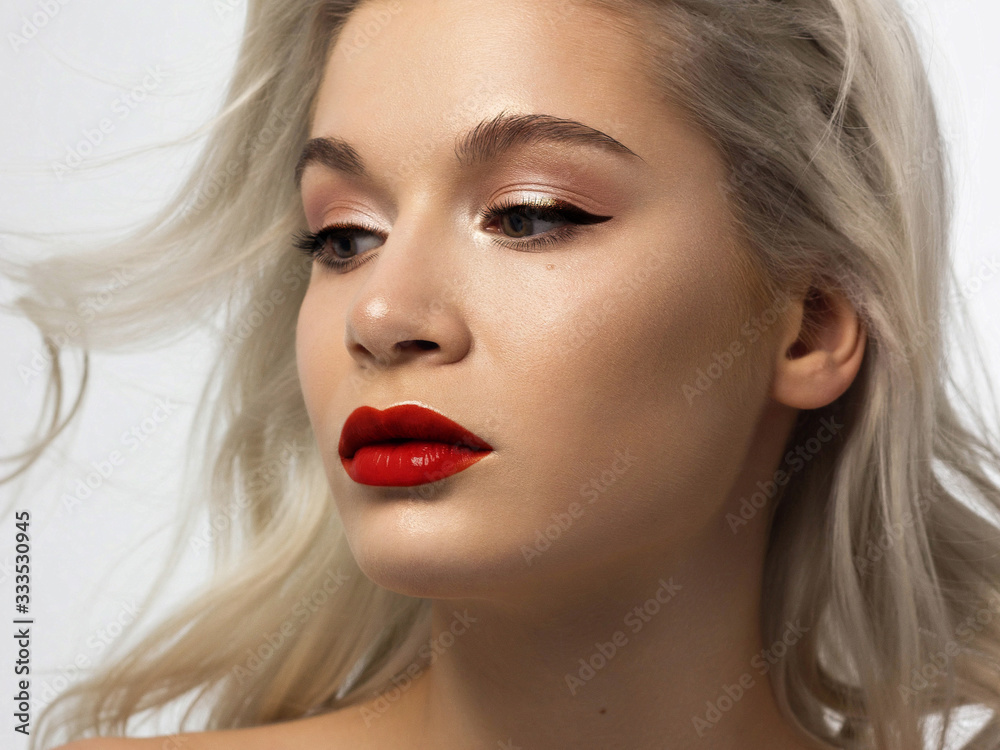 Fototapeta premium Closeup portrait of a woman with developing straight hair. Sweet tender young girl blonde. Red lipstick, transparent clean skin. Skin care natural cosmetics in the spa salon or cosmetology.