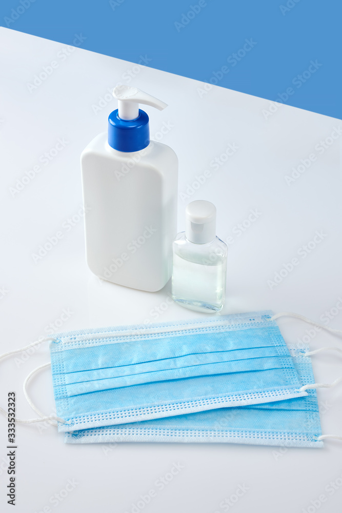 White antiseptic bottle with dispenser next to hand sanitizer and two blue medicine masks on white acrylic table. Blue background, vertical shot White antiseptic bottle with dispenser next to hand sanitizer and two blue medicine masks on white acrylic table. Blue background, vertical shot