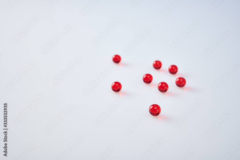 Red round vitamin capsules on white acrylic background
