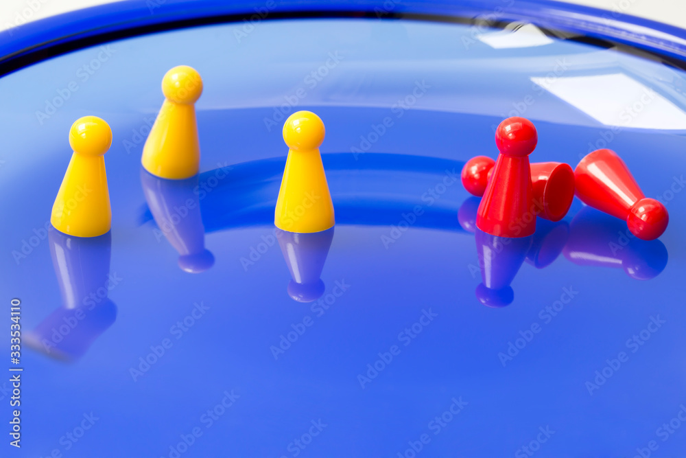 Obraz premium Social distancing concept. Three yellow game pieces keeping distance and three red game pieces grouped, two of them fallen down