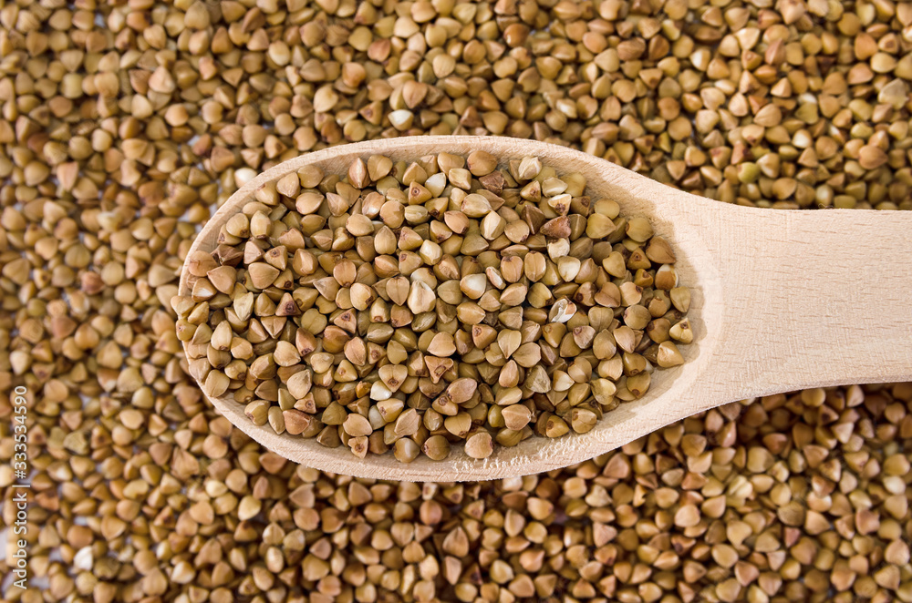 buckwheat in a wooden spoon against the background of buckwheat. Close-up. View from above. buckwheat in a wooden spoon against the background of buckwheat. Close-up. View from above.