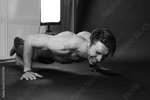 Muscular man doing push-ups on one hand against dark background.