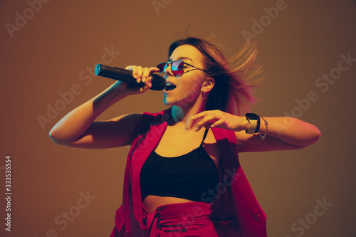 Young caucasian musician, performer singing on gradient background in neon light. Concept of music, hobby, festival. Joyful woman party host, DJ, singer, band's front artist. Colorful portrait. photo