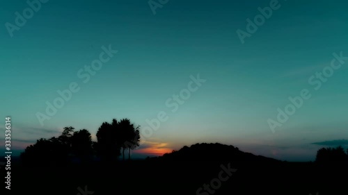 Large sun disc move down, hiding behind a hill with dark bushes. photo