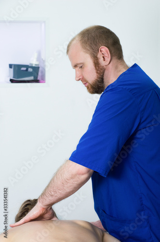 Portrait of a young male doctor. Man in blue doctor uniform is doing back massage to a woman