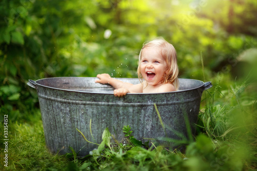 girl bathing in a basin on the street, water splashes, summer in the village, happy childhood, children's laughter