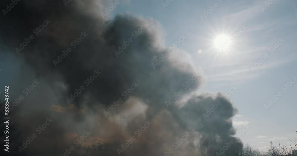 Clouds smoke and fire in city park on blue sky slow motion, bright sun disk, lens flare arson on background of trees in spring. Protest, criminal incident. Consequences of flaming flame park Clouds smoke and fire in city park on blue sky slow motion, bright sun disk, lens flare arson on background of trees in spring. Protest, criminal incident. Consequences of flaming flame park