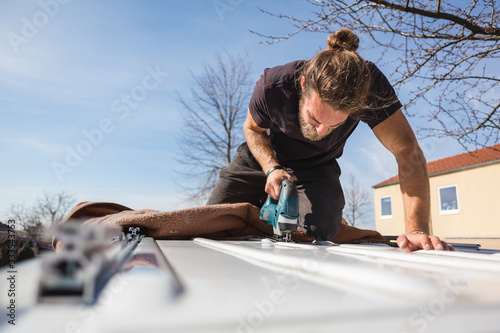Man using a jigsaw to saw into the roof of a van