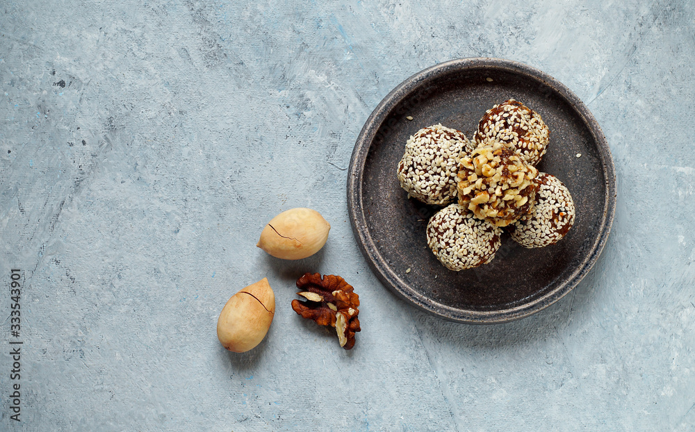 Fototapeta premium Oatmeal, energy balls covered with sesame and walnut crumbs, lie on a ceramic plate, next to pecans . Top view, copy space, healthy food, trend..