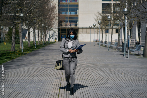 Fototapeta Naklejka Na Ścianę i Meble -  Girl putting on a protective mask to avoid contagion while walking down the street. Coronavirus concept