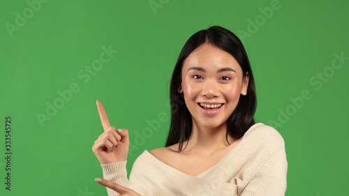 Young asian woman pointing up with hand gesture isolated on green background