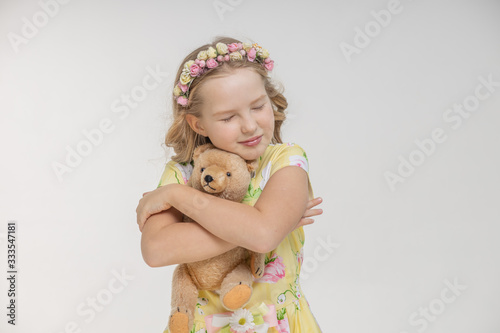 Young blonde woman hugs her teddy bear with tenderness to the cozy warmth, closing her eyes on an isolated white background