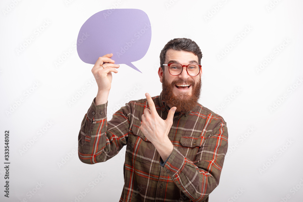Photo of cheerful young man with beard wearing glasses and pointing at bubble speech Photo of cheerful young man with beard wearing glasses and pointing at bubble speech