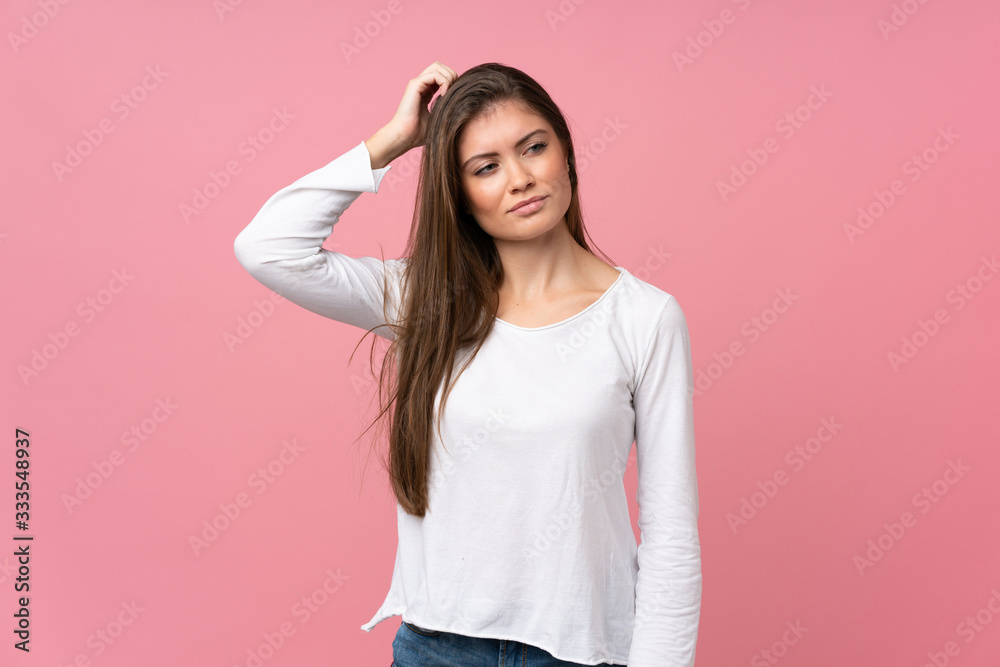 Young woman over isolated pink background having doubts while scratching head Young woman over isolated pink background having doubts while scratching head