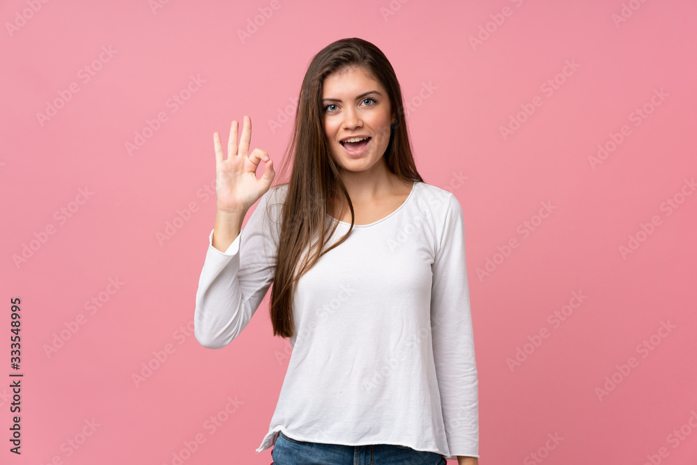 Young woman over isolated pink background surprised and showing ok sign Young woman over isolated pink background surprised and showing ok sign