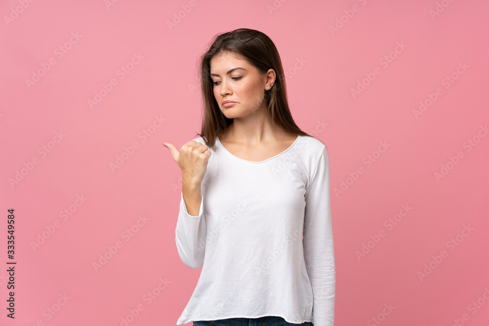 Young woman over isolated pink background unhappy and pointing to the side Young woman over isolated pink background unhappy and pointing to the side