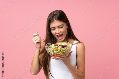 Young woman with salad over isolated pink wall
