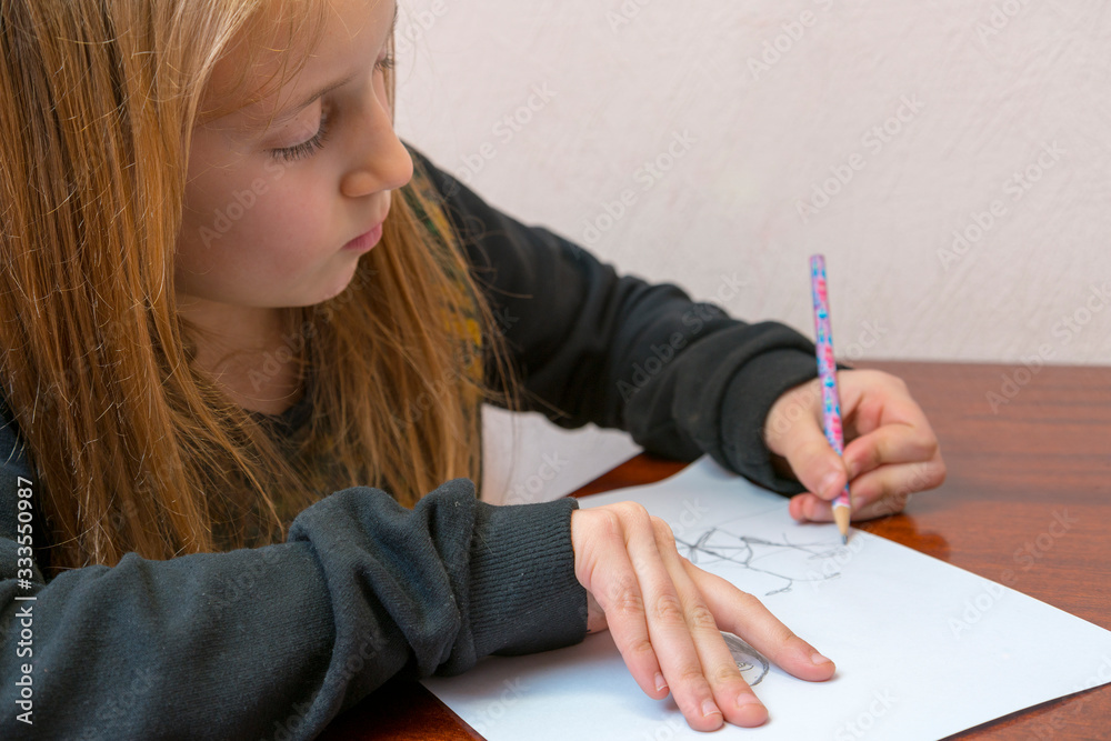 Schoolgirl draws at a desk. Little girl student studying sitting at her desk. School, education, knowledge and children. toned Schoolgirl draws at a desk. Little girl student studying sitting at her desk. School, education, knowledge and children. toned