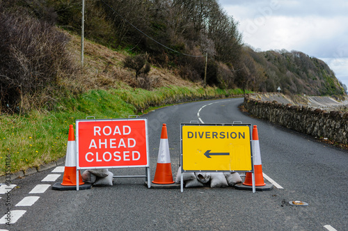 Road closed signs on a coastal road due to fallen rocks.