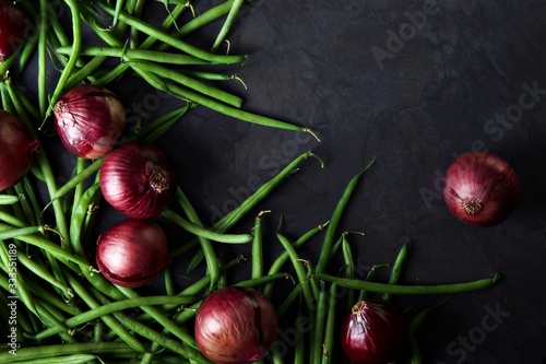 Φωτογραφία Green beans and red onions scattered across a dark grey background