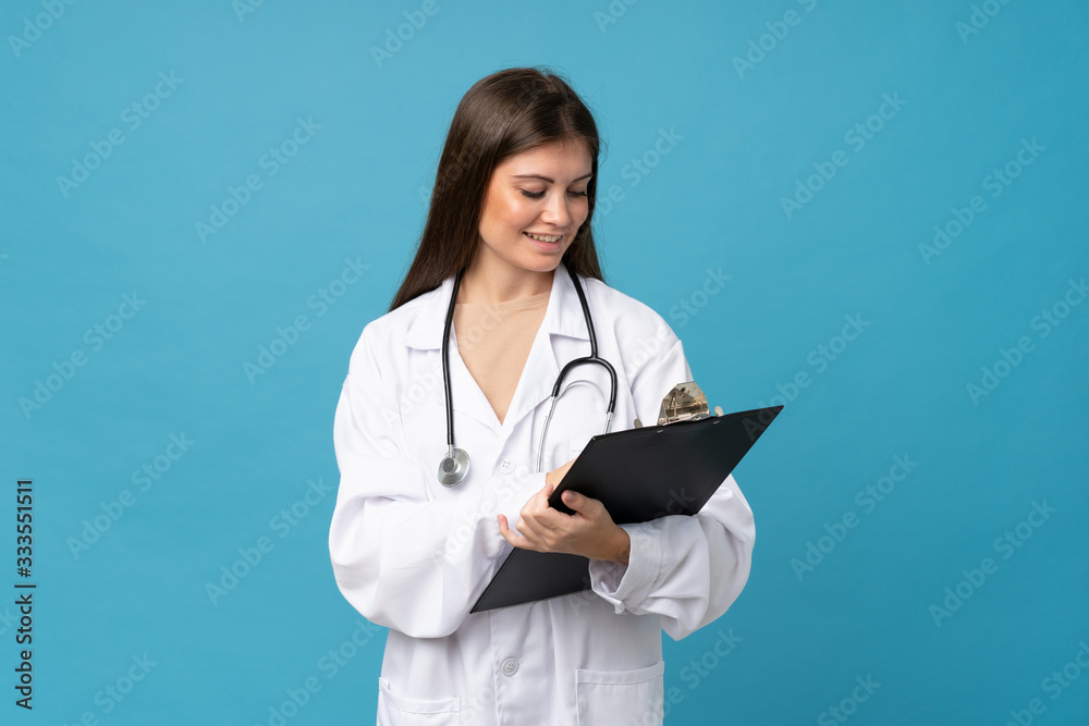 Young woman over isolated blue background with doctor gown and writing in a folder