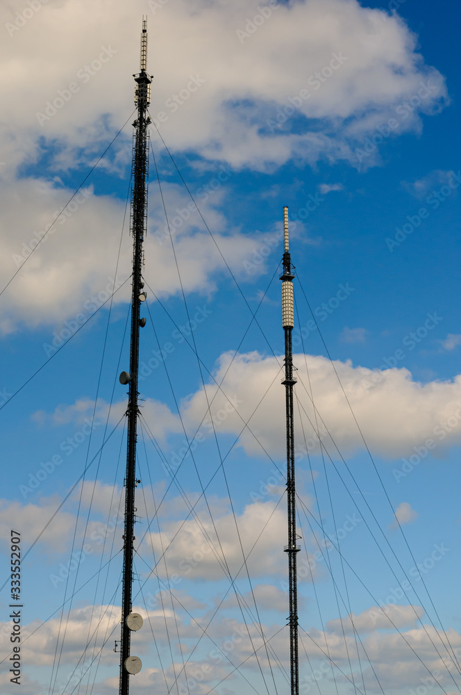 Obraz premium Two UK television and radio masts against a blue sky with clouds.