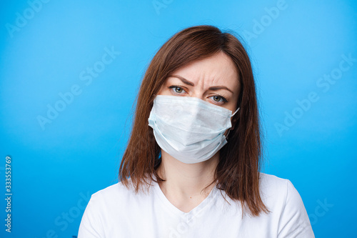 Stock photo of a brunette woman in aseptic mask and white t-shirt looking at camera with disapproval and disbelief.
